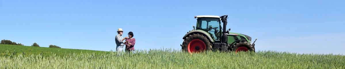 two farmers speaking in a field next to a tractor